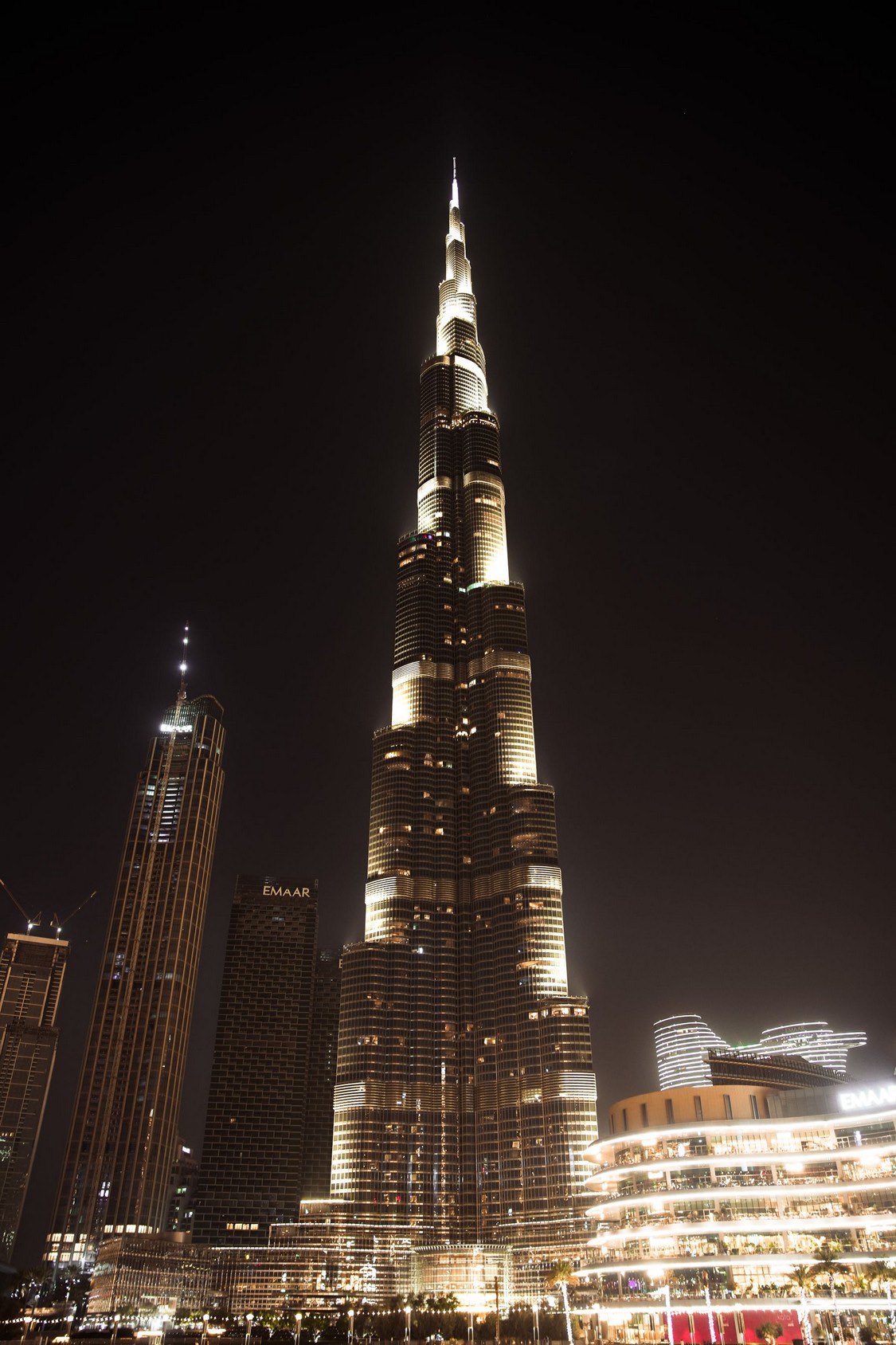 The Burj Khalifa lit up at night, seen from below with Downtown Dubai buildings at its base.