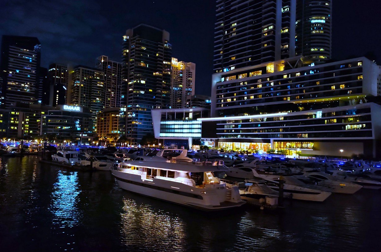 Yachts moored in a Dubai marina at night, in front of lit apartment towers.